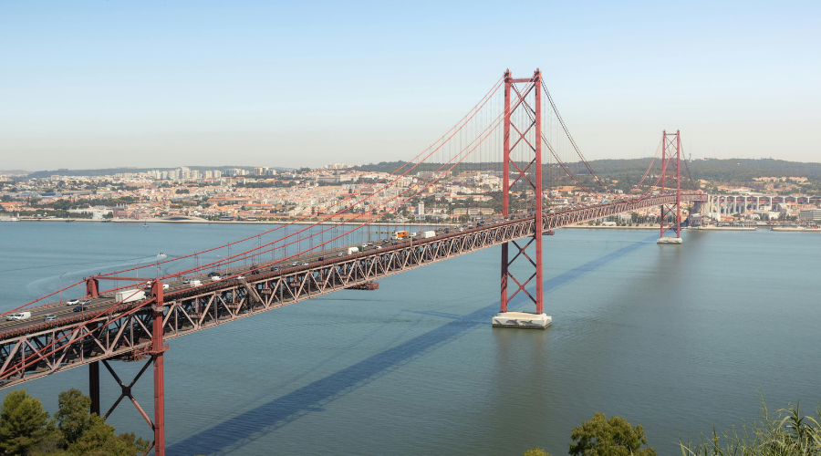 红色吊桥横跨一条宽阔的河流,桥上车水马龙,从高处俯瞰,背景是一座城市。