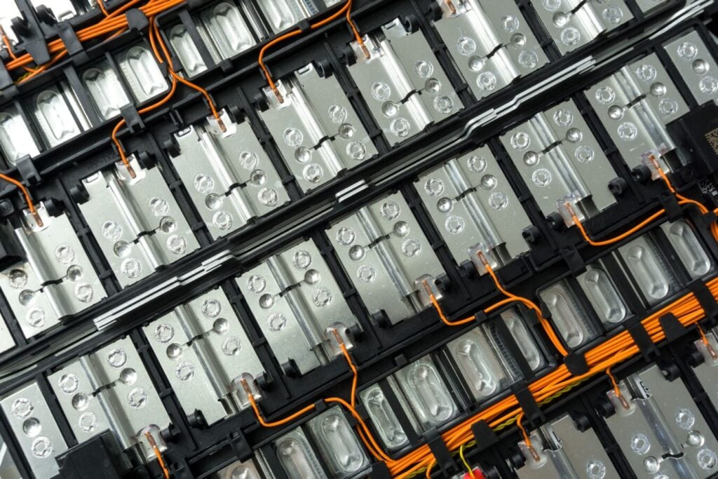 Vue rapprochée d'une batterie montrant des rangées d'éléments de batterie interconnectés, des barres omnibus métalliques et un câblage électrique orange.
